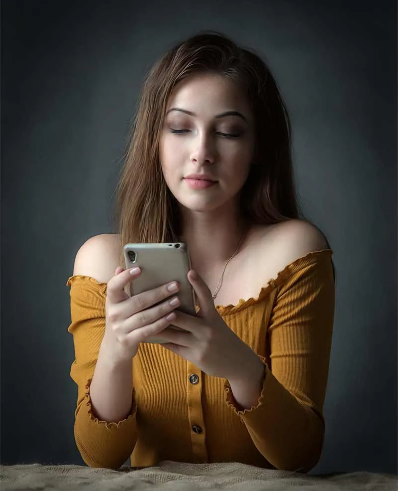 Jente i gul genser ser konsentrert på mobiltelefonen