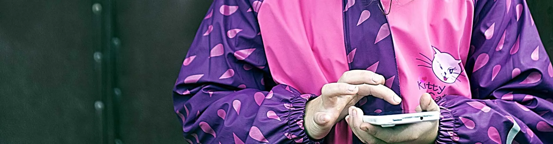 Barn i rosa og lilla regnjakke med kattemotiv bruker mobiltelefon