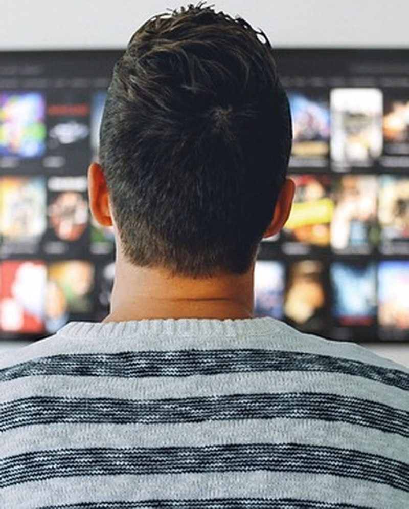 Mann sett bakfra foran en TV med strømmetjenestens filmoversikt